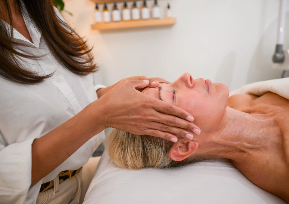 A By Karisse esthetician working with both hands along a client's temples and jaw during a facial